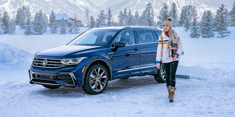 A woman standing next to a 2023 Volkswagen Tiguan in the snow.