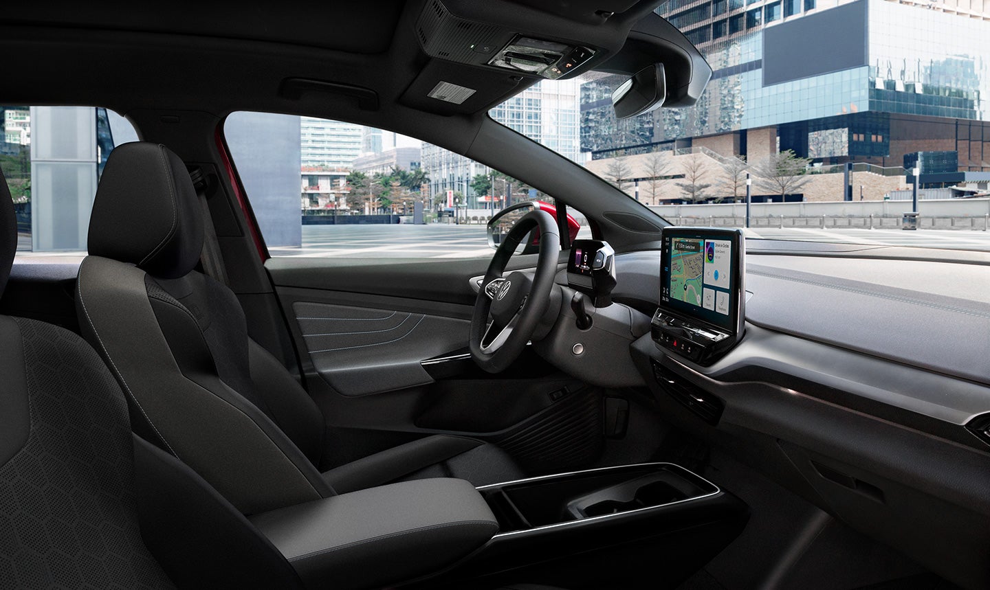 An interior view of the driver area in an ID.4 AWD Pro S Plus, showing the driver seat, steering wheel, dashboard, and center console display. A modern, downtown city can be seen through the windows.